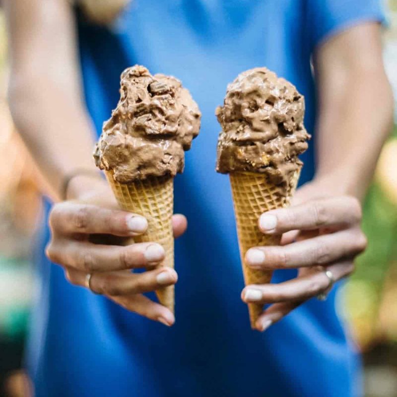 Person holding two chocolate ice cream cones.